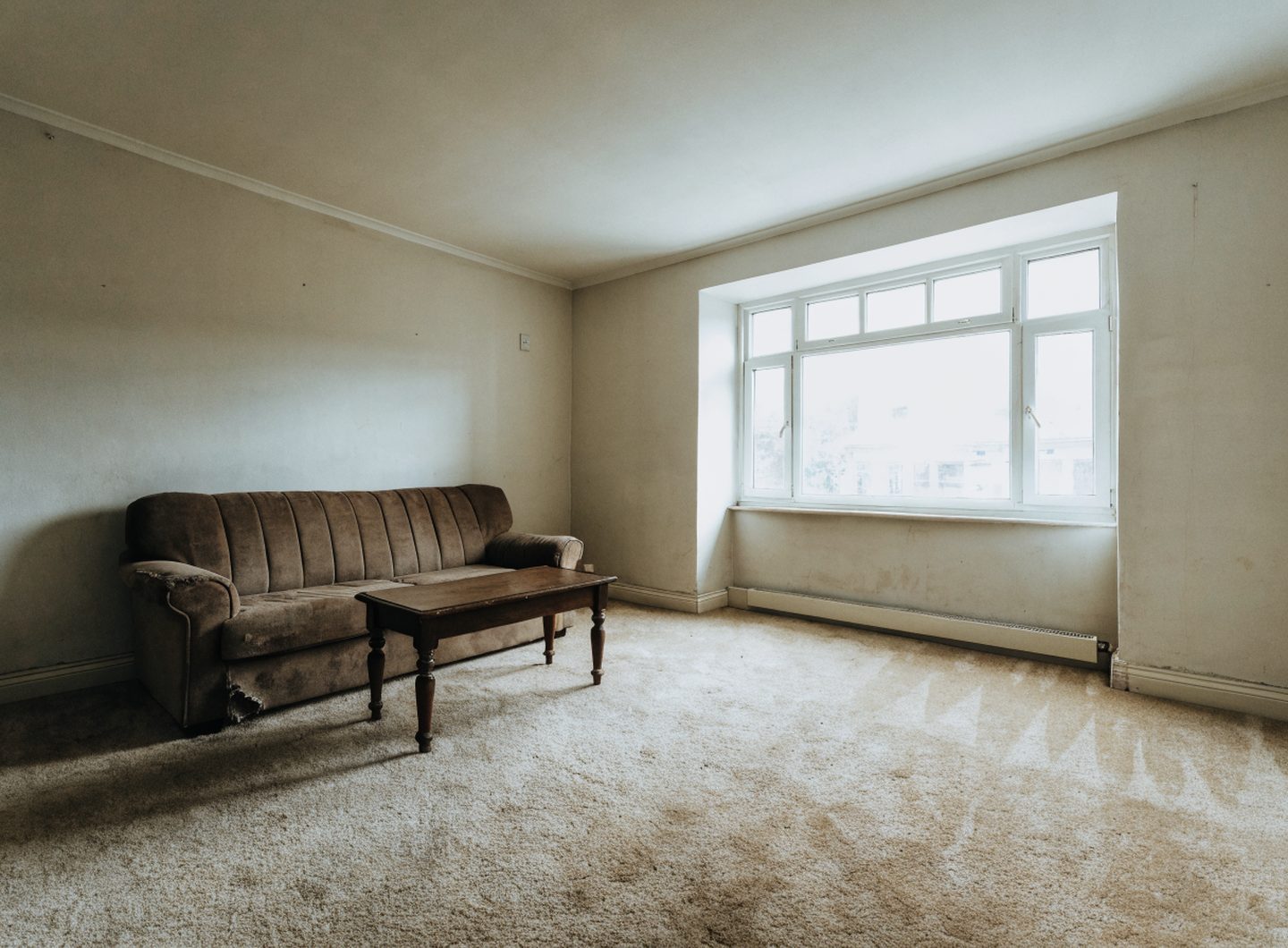 A dated living room with a worn brown sofa and beige carpet